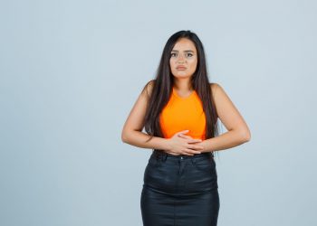 beautiful girl keeping hands on stomach in orange top and skirt and looking painful , front view.