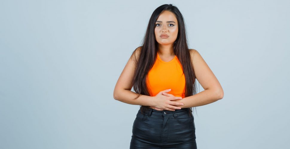 beautiful girl keeping hands on stomach in orange top and skirt and looking painful , front view.